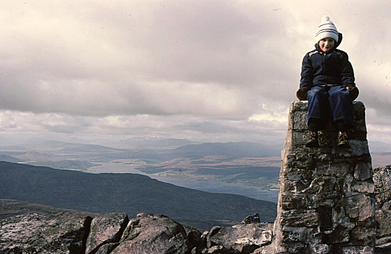 Child sitting on the trig point on the Schiehallion peak